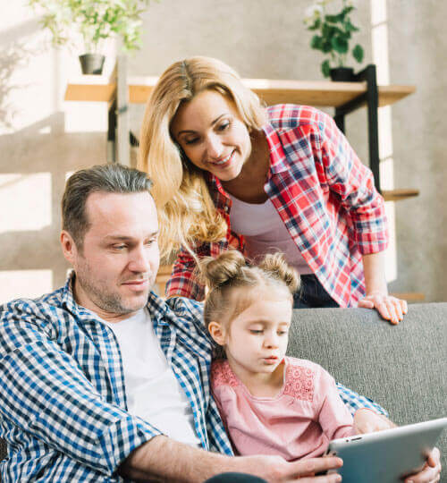 Vater, Mutter und Tochter sitzen zuhause auf dem Sofa und schauen gemeinsam auf ein Tablet