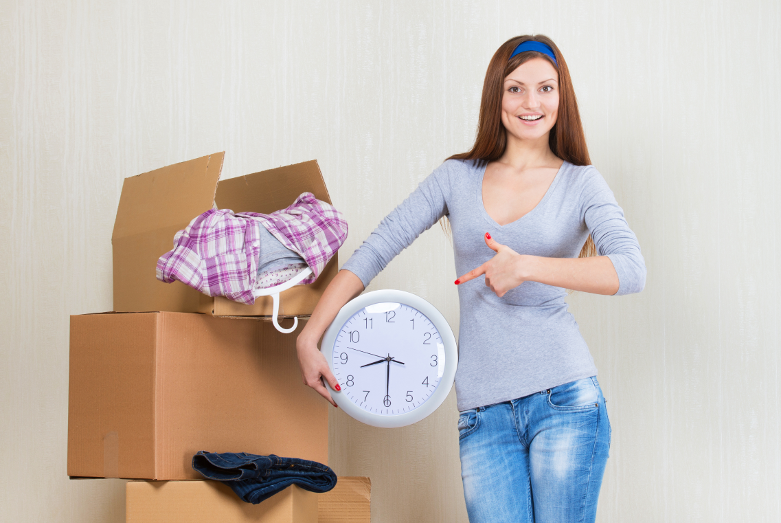 smiling woman with clock sitting floor among moving boxes 1 1