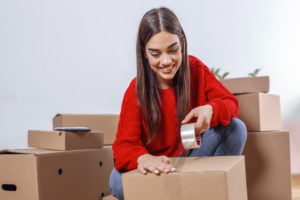 young woman packing boxes moving new apartment young woman moving new place repair concept happy young woman with many cardboard boxes sitting floor